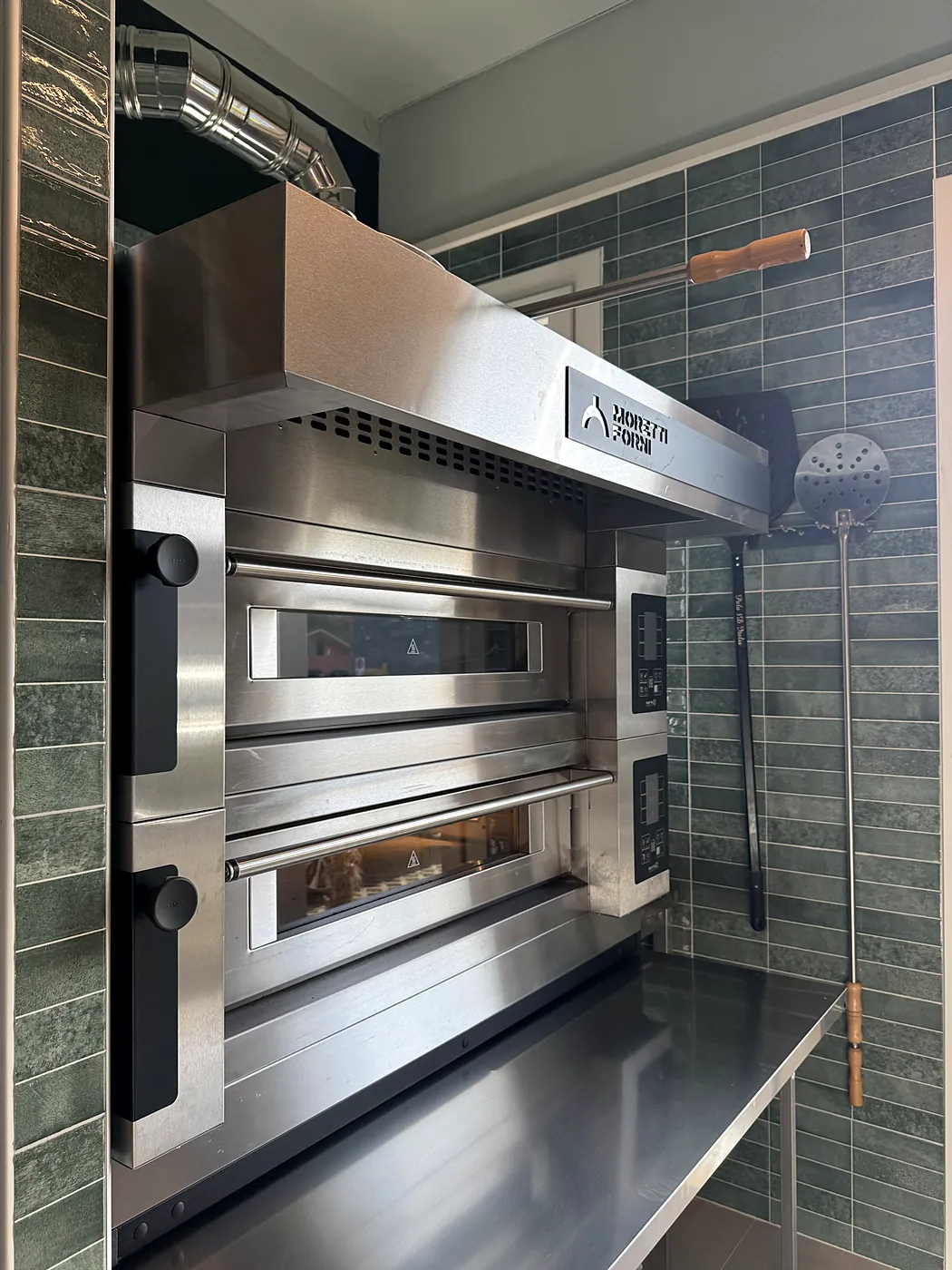 Il forno per le pizze, con le pale appese alla parete di piastrelle verdi